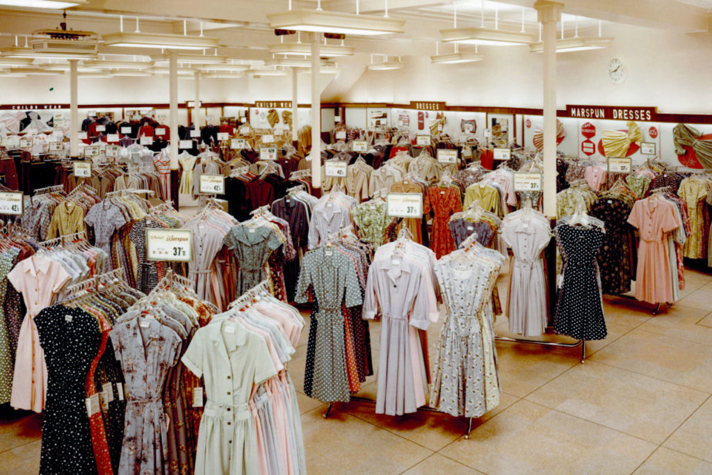 Colour image of dresses on rails in a store.