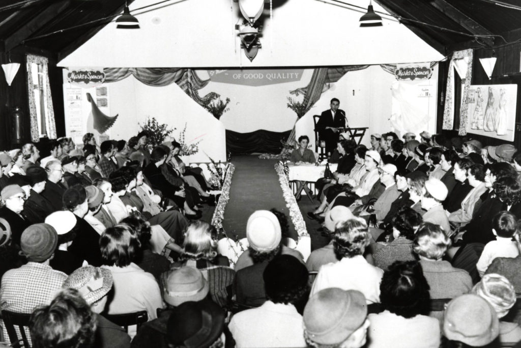 Black and white image of a stage and audience seated around a catwalk.