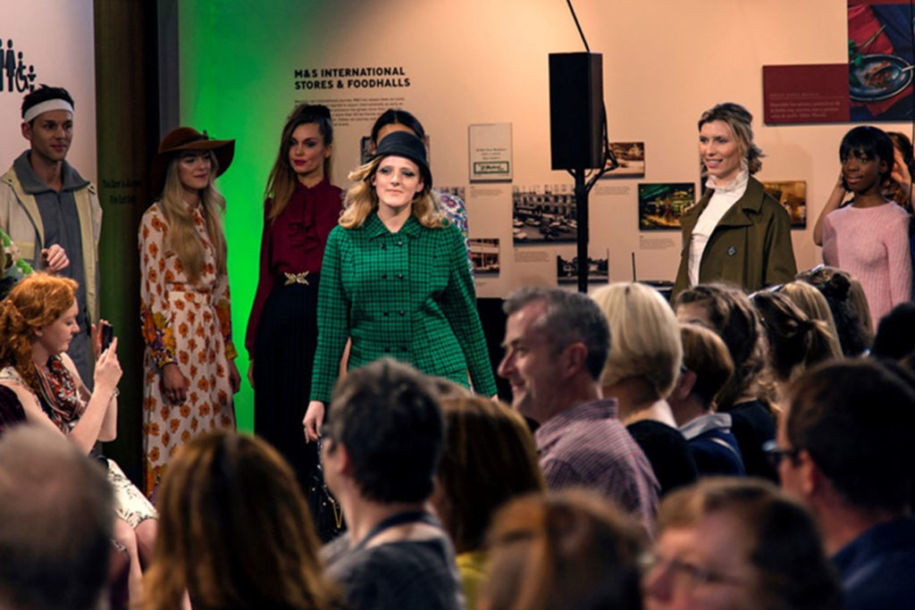 A colour image of models on a catwalk with an audience.