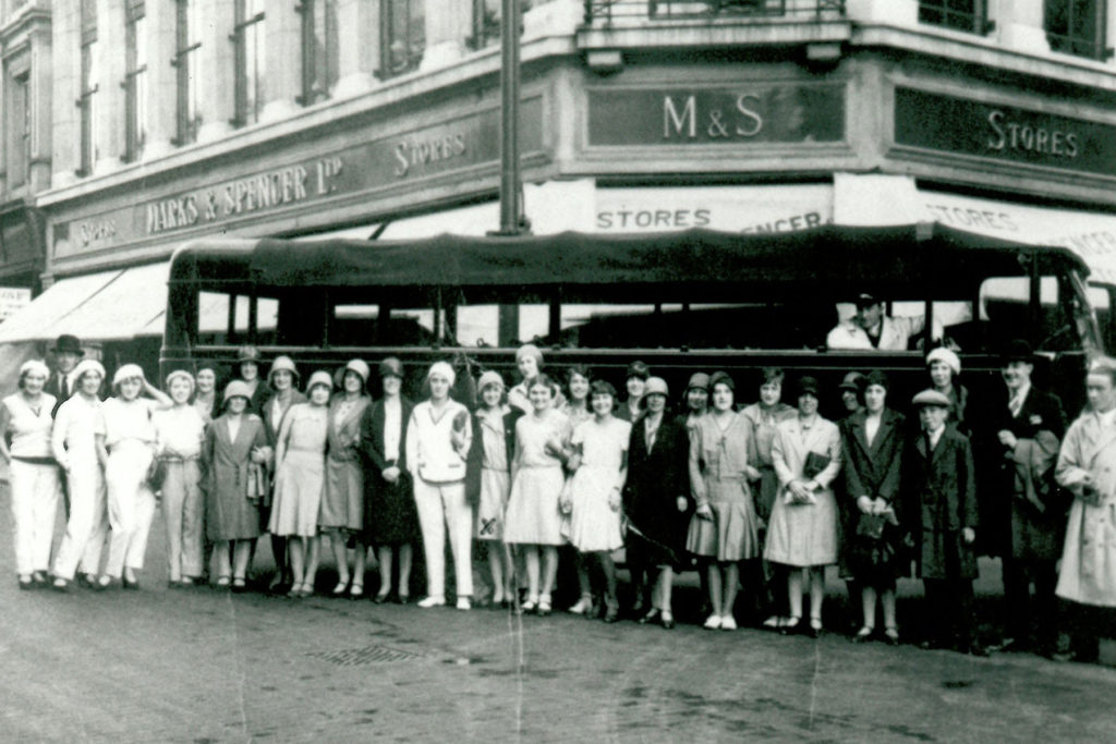 A black and white image of a group of people standing in front of a bus.