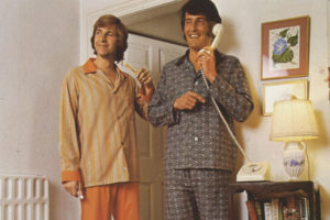 A colour image of two male models in pyjamas, one is on the phone.