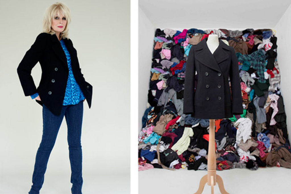 A colour image of a black coat in front of a pile of clothing and Joanna Lumley.