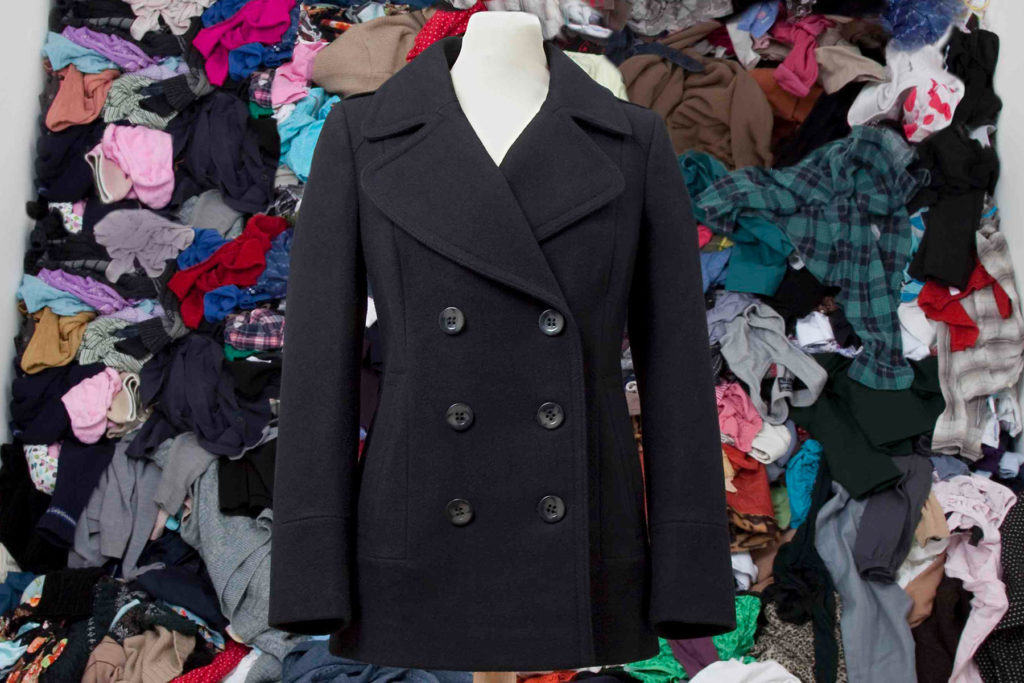 A colour image of a black coat in front of a pile of clothing.