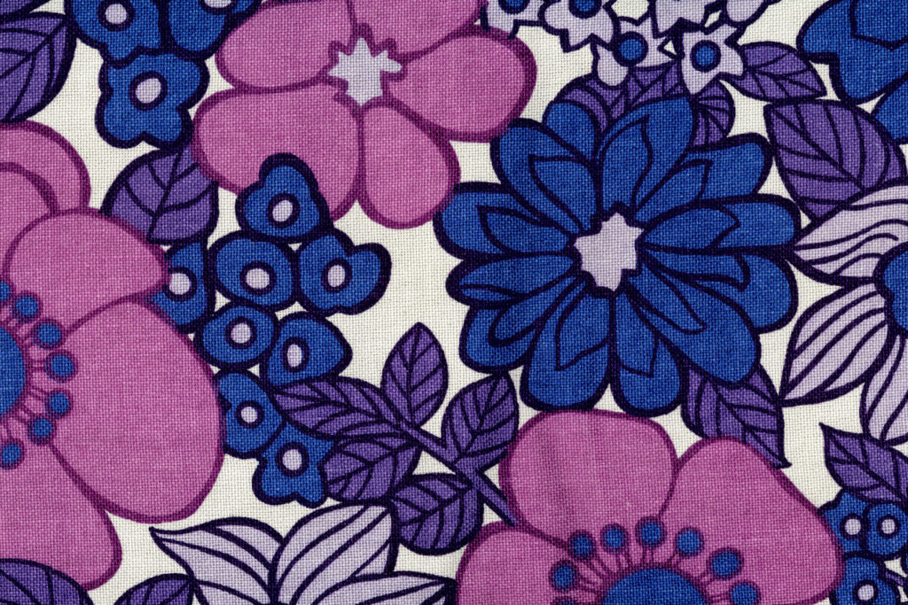 A close up image of a printed fabric with a blue, purple and pink bold floral design.