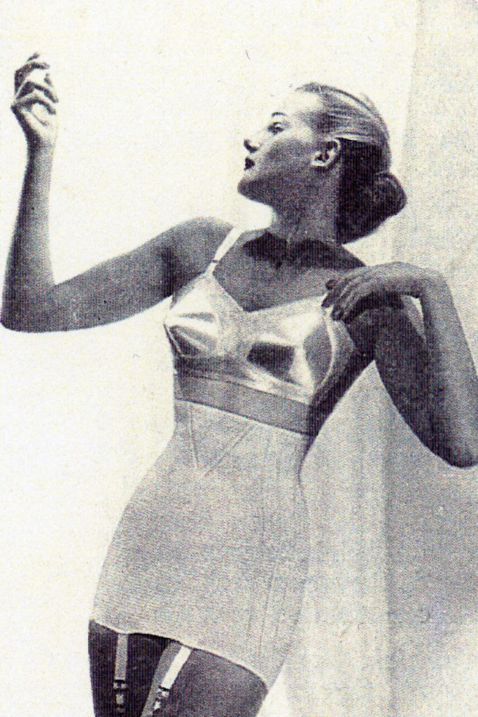 A black and white image of a female model in a bra and girdle.