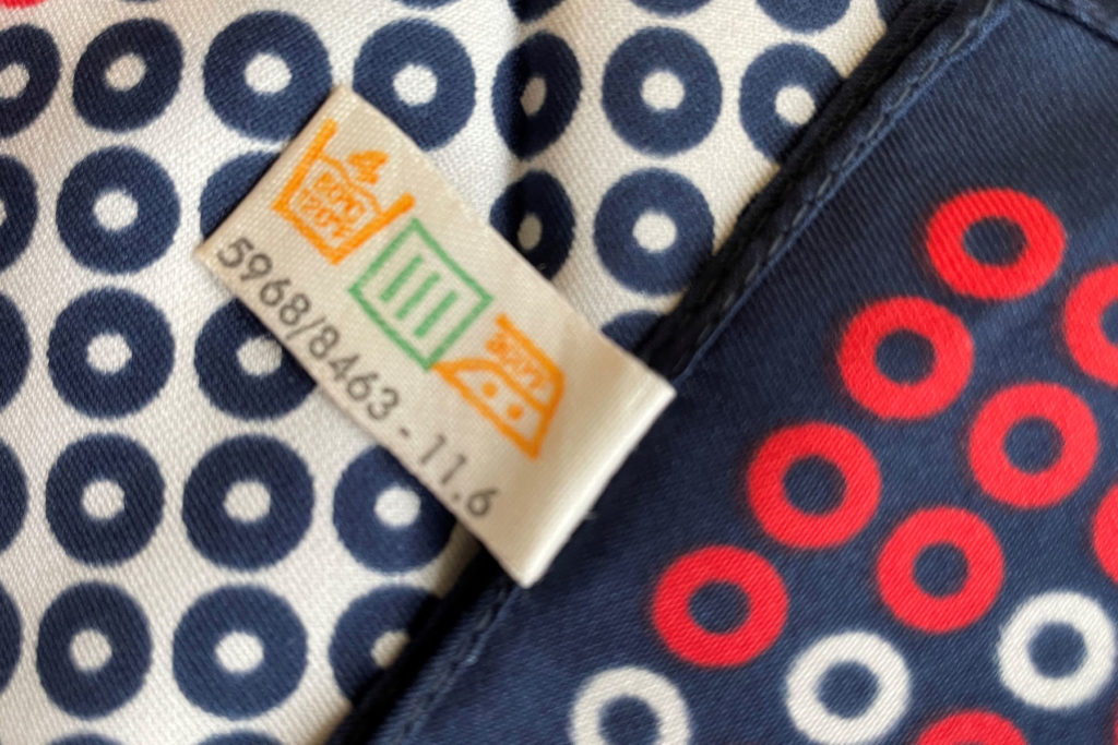 A colour image of a navy headscarf with red and white circle design showing the care label.