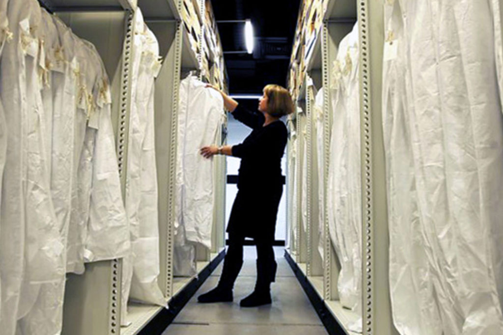A colour image of a person standing in the aisle of some archive clothing racks.