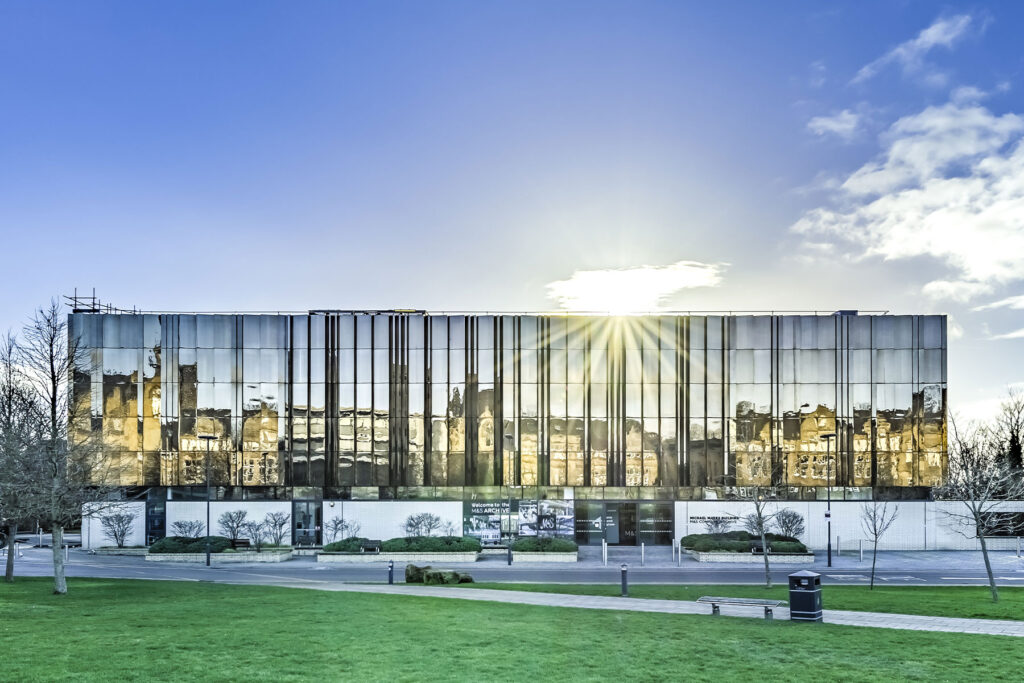 colour photo of a large metallic building with sun rising behind it