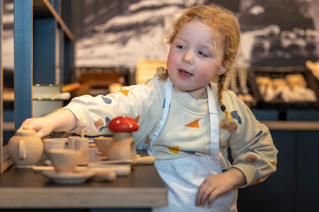 colour image of a young child in a white apron playing with wooden toys