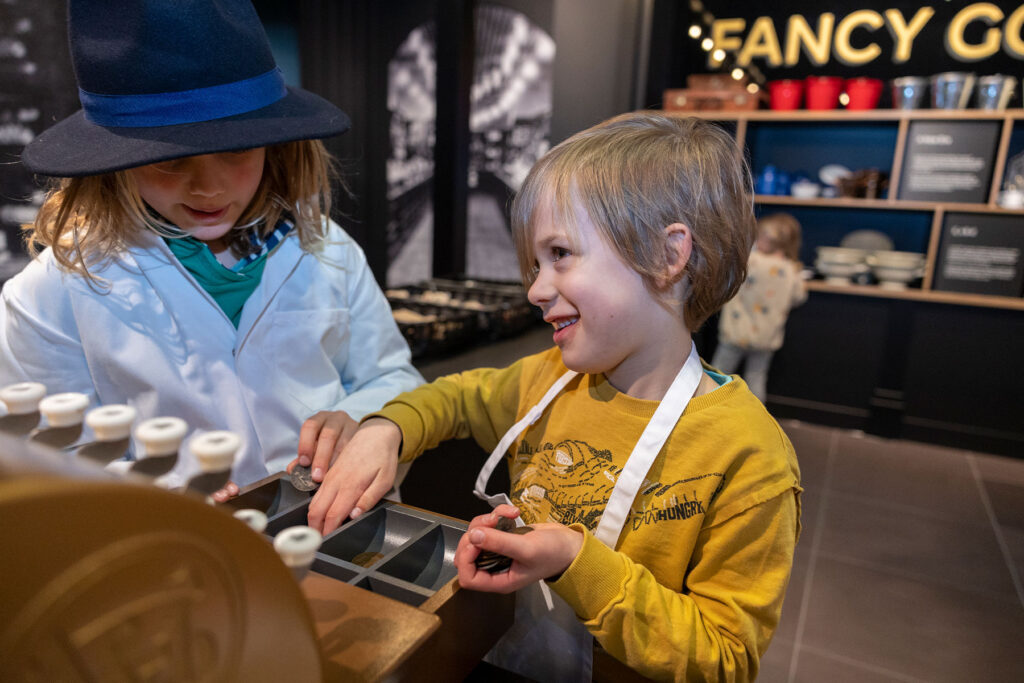 Colour image of two children playing in a pretend shop with a till