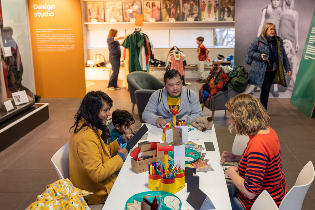 colour image of people sitting at a table with craft materials in a museum