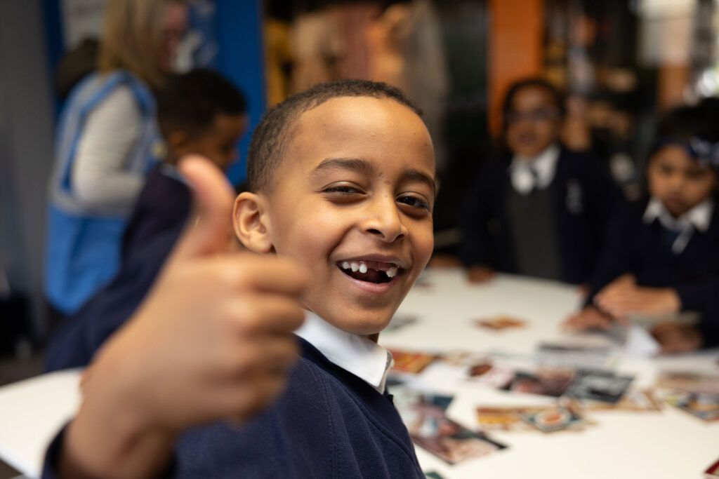 Colour image of a school pupil smiling and giving a thumbs up