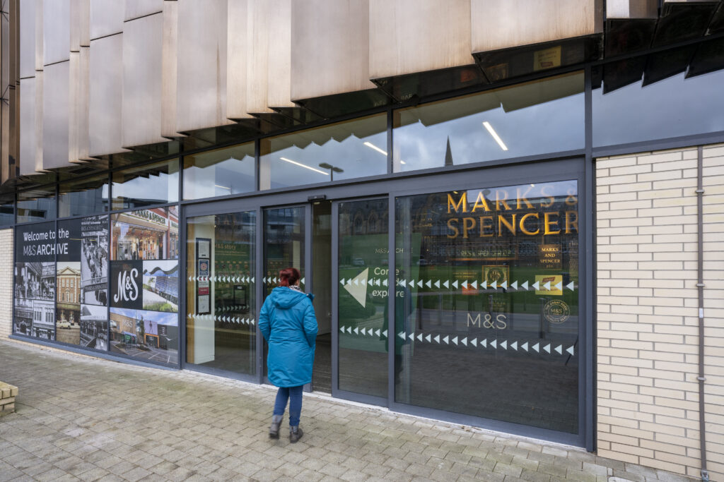 Colour photo of a person walking into a building with sliding glass doors.